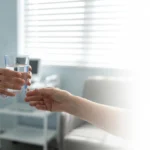 Roke zdravstvenega strokovnjaka ponujajo kozarec vode v mirnem kliničnem okolju – odtegnitveni sindrom, varni prvi koraki